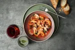 Luzerne Smokey Plum share bowl in use, filled with seafood stew on a sage-green charger plate