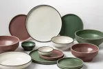 Luzerne Share Bowl in smoky plum with speckled glaze, shown in a collection with cream and green plates and bowls.