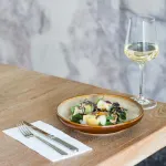 Luzerne oval share bowl in use, filled with salad, featuring a cream interior and glossy amber-brown rim.