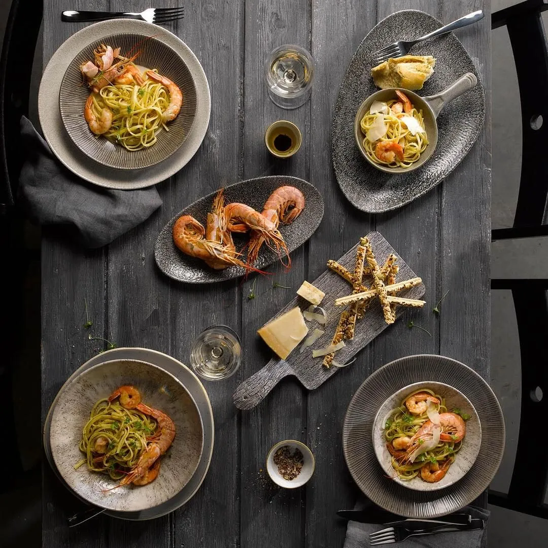 Churchill round coupe plate in use on a dining table, holding shrimp and green pasta alongside a grey platter of prawns.
