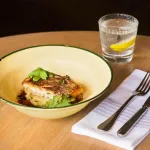 Luzerne Round Plate 170mm in use, cream enamel bowl with green rim holding seared fish on mashed potato