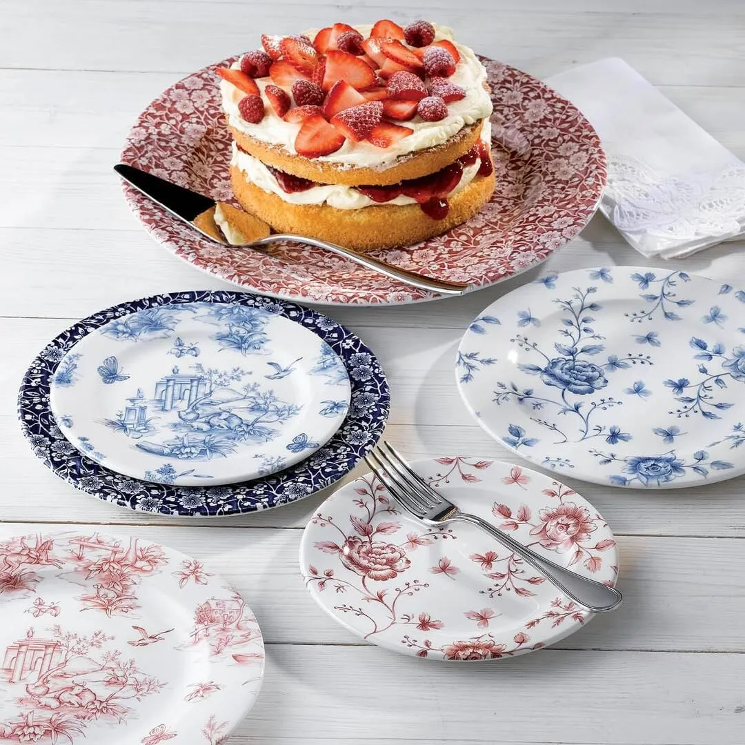 Churchill Prague Toile ceramic plates in red and blue patterns, shown in use with a strawberry cake and fork on a white table.