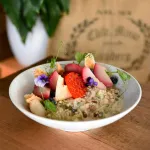 Luzerne round bowl in use, filled with a fruit salad, showing its wide rim and matte speckled light-grey finish.